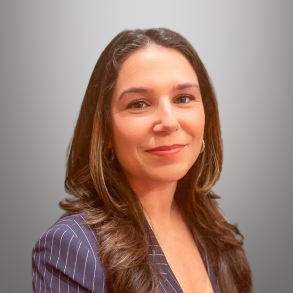 Professional headshot of Shannon Simonelli, featuring a confident expression and business attire against a neutral gradient background.