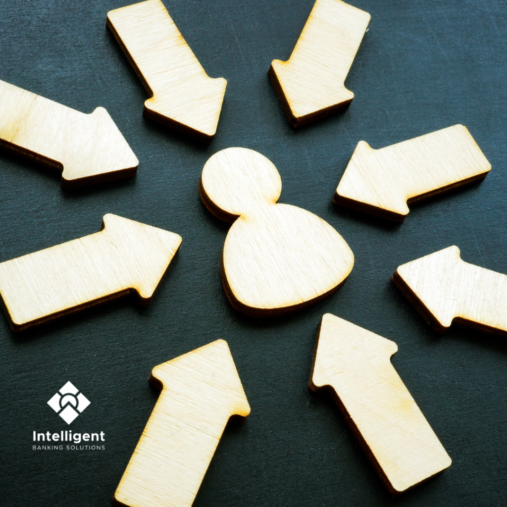 Wooden figure surrounded by directional arrows on a dark background, symbolizing a strategic approach to debt recovery. Featured image for the blog post 'Redefining Debt Recovery' by Intelligent Banking Solutions.